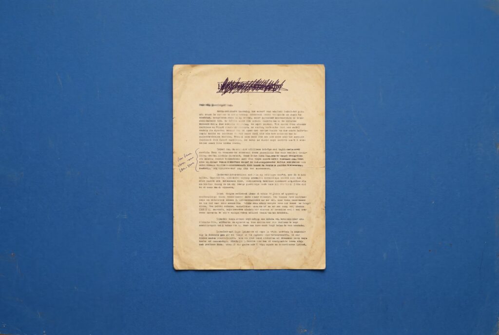 Oud getypt document met doorgekraste titel en handgeschreven aantekeningen in de kantlijn, op een blauwe achtergrond